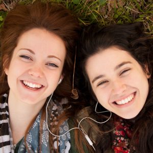Two happy teenage girls lying on the grass sharing earphones