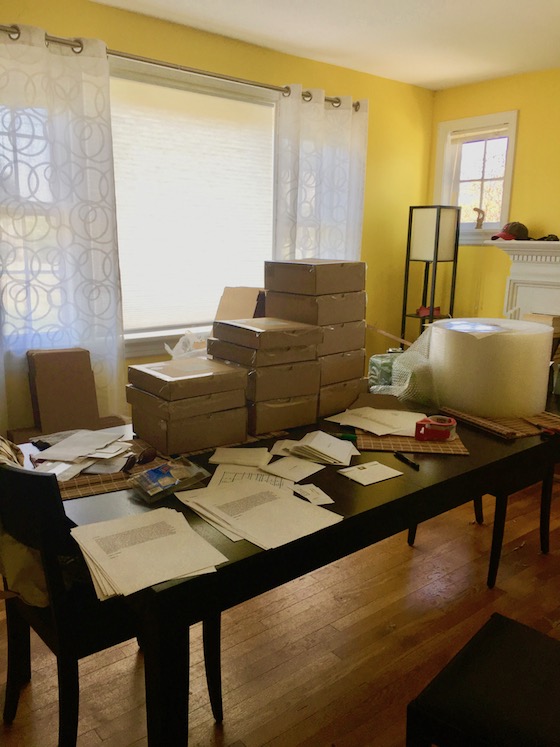 a large dining room table covered in cardboard boxes, mailing lablels, and bubble wrap