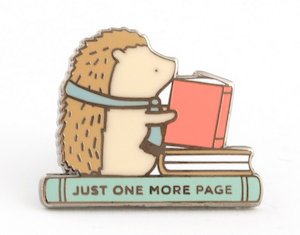 an enamel pin of a hedgehog sitting on a book reading a book with the spine saying "Just one more page"
