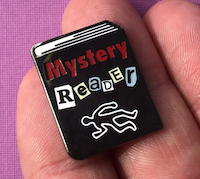 enamel pin of a black book with Mystery Reader and the outline of a body on the cover
