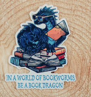 sticker of a blue dragon reading books with the text "in a world of bookworms be a book dragon"
