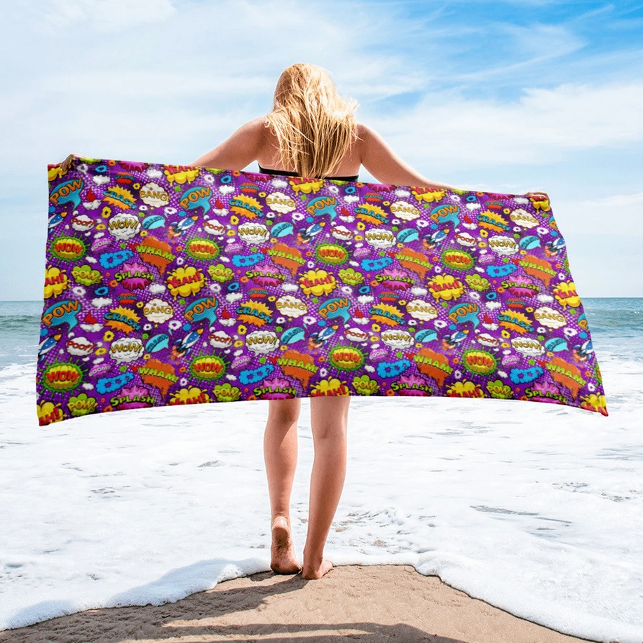 A woman holds a beach towel covered in comic book-style onomateopoeias