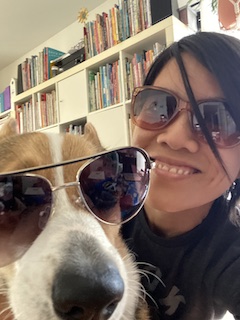 Karina and her tri-color corgi Lalo wearing sunglasses with a bookshelf full of picture books in the background.