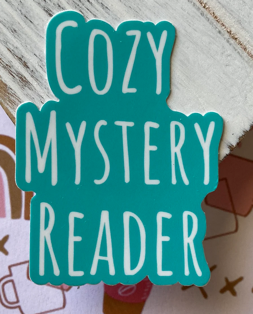 a die cut teal sticker that says in white letters "cozy mystery reader"