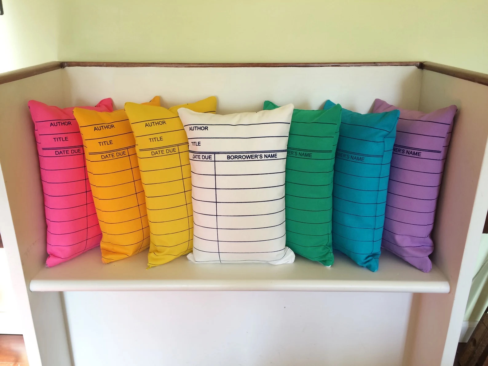 A photo of a set of pillows this look like library cards. The pillows come in all color of the rainbow.