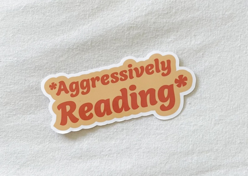 sticker with the words "aggressively reading" in orange.