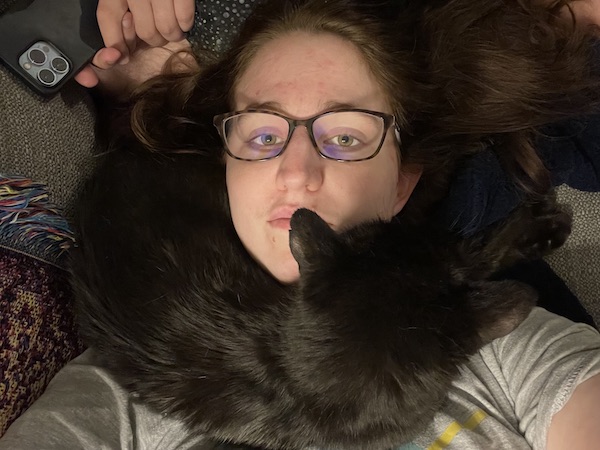 brown-haired woman laying down with a black cat laying across her neck like a scarf
