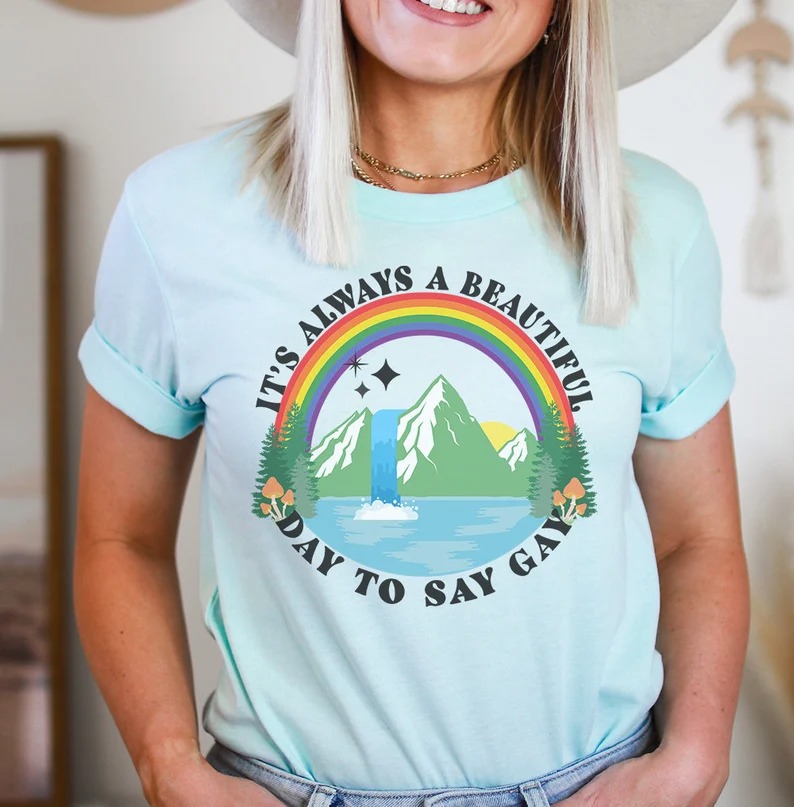 a photo of someone wearing a shirt with a rainbow over a mountain and the text "It's always a beautiful day to say gay"