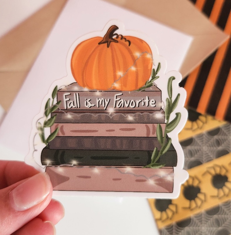 a sticker featuring a stack of fall-colored books and a pumpkin that reads "fall is my favorite."