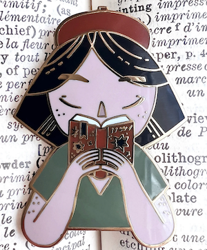 enamel pin of person's bust with black hair reading a book