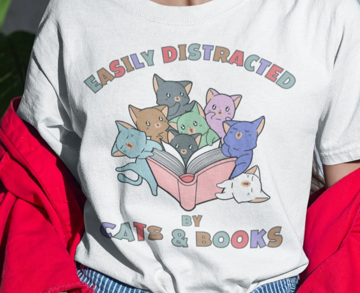 T-shirt with cats reading a book. Text says "Easily Distracted by Cats and Books"