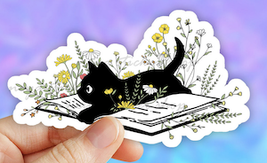 sticker of black kitten laying in center of open book surrounded by flowers