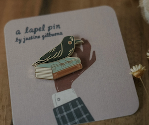 enamel pin of a raven sitting on two books
