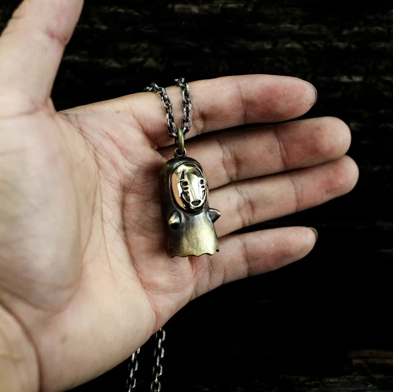 a photo of a hand holding a silver No Face pendant