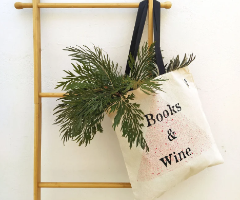 Cream colored tote bag with a red speckled triangle in the center and the words "Books & Wine"