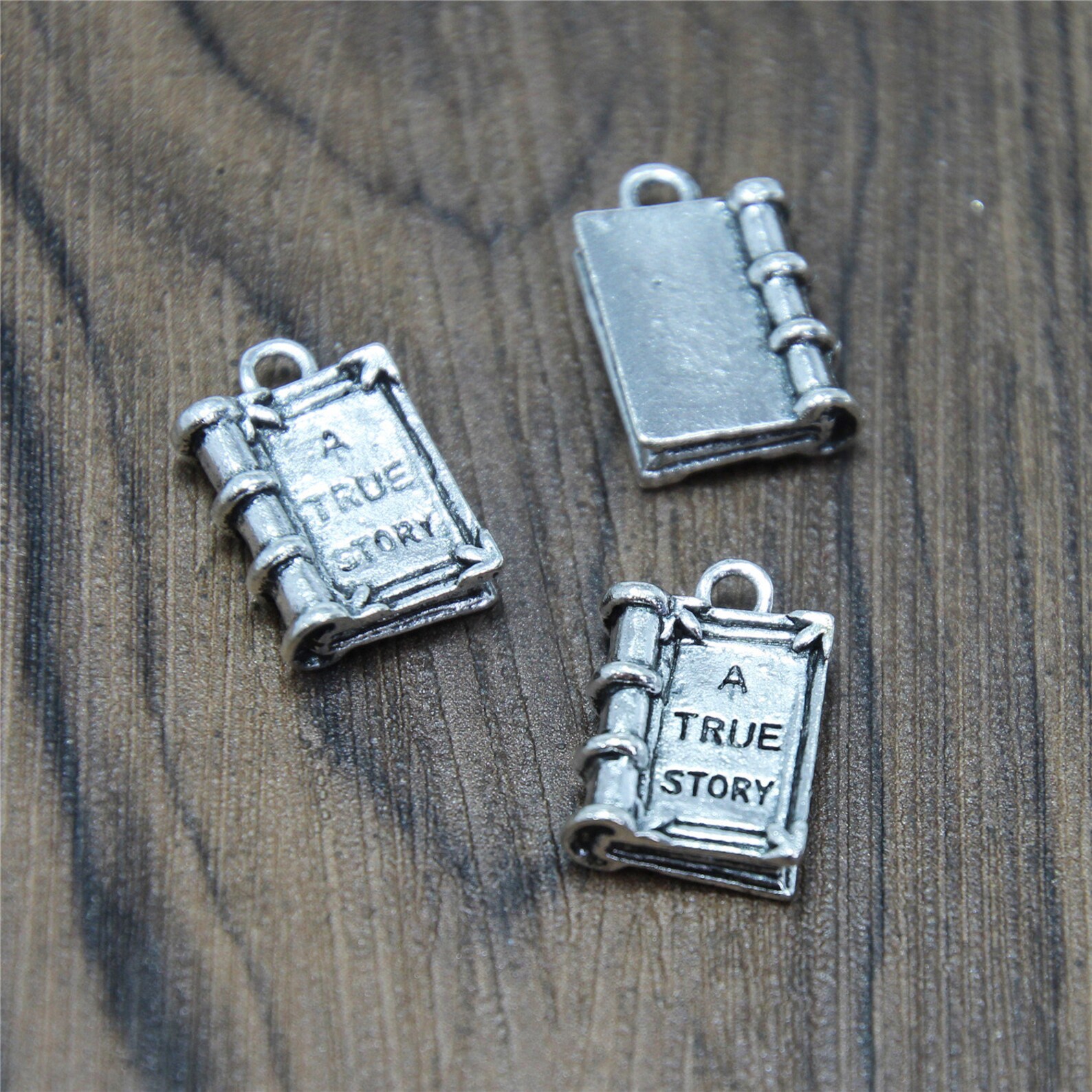 A photo of a silver book charm that says "True Story" on the front