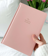 a light pink journal that says the reading journal on the cover in gold