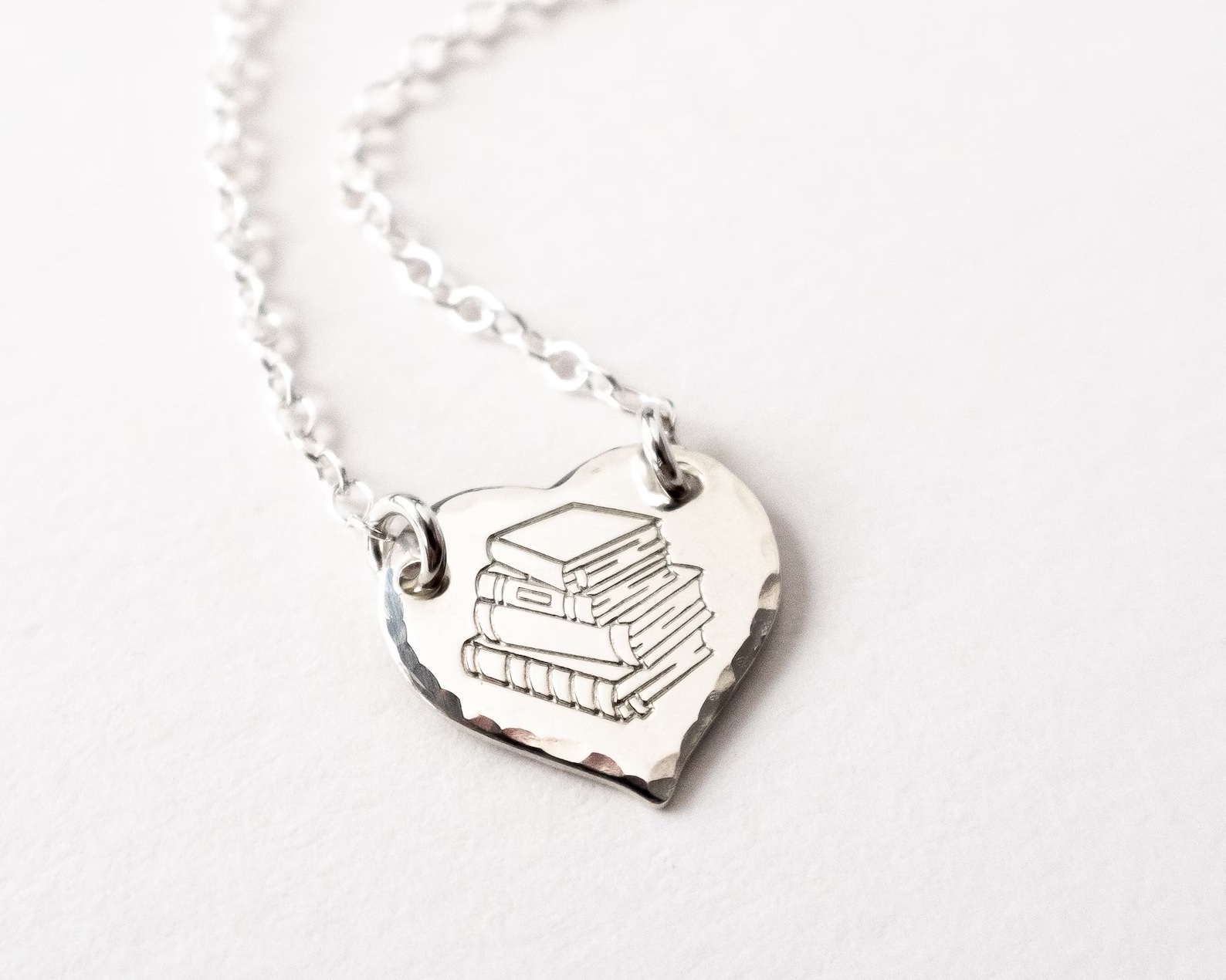 a photo of a silver heat pendant engraved with the image of a stack of books