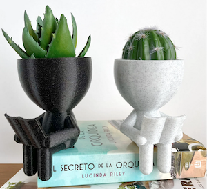 little planters carved to look like people reading with succulant going on top of head