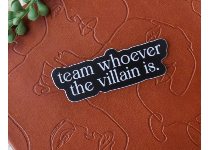 Image of a black and white sticker. It reads "team whoever the villain is."