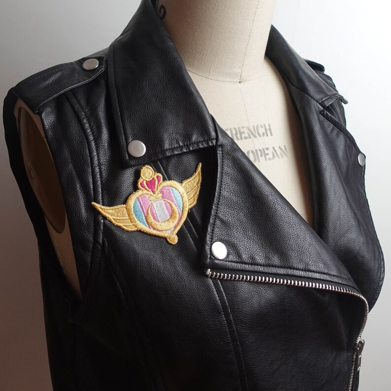 a patch with a Sailor Moon transformation compact with a trans pride on the background. It's on a leather jacket.