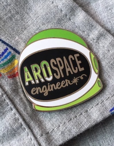 a pin of a space helmet in aromantic pride colors and the text AroSpace Engineer