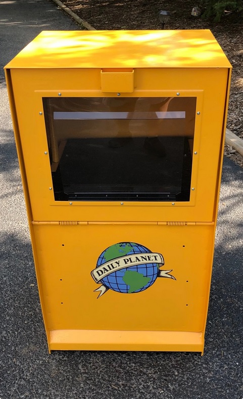 A yellow newspaper box with the Daily Planet logo