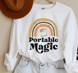 sweatshirt with a rainbow and book that says "portable magic"