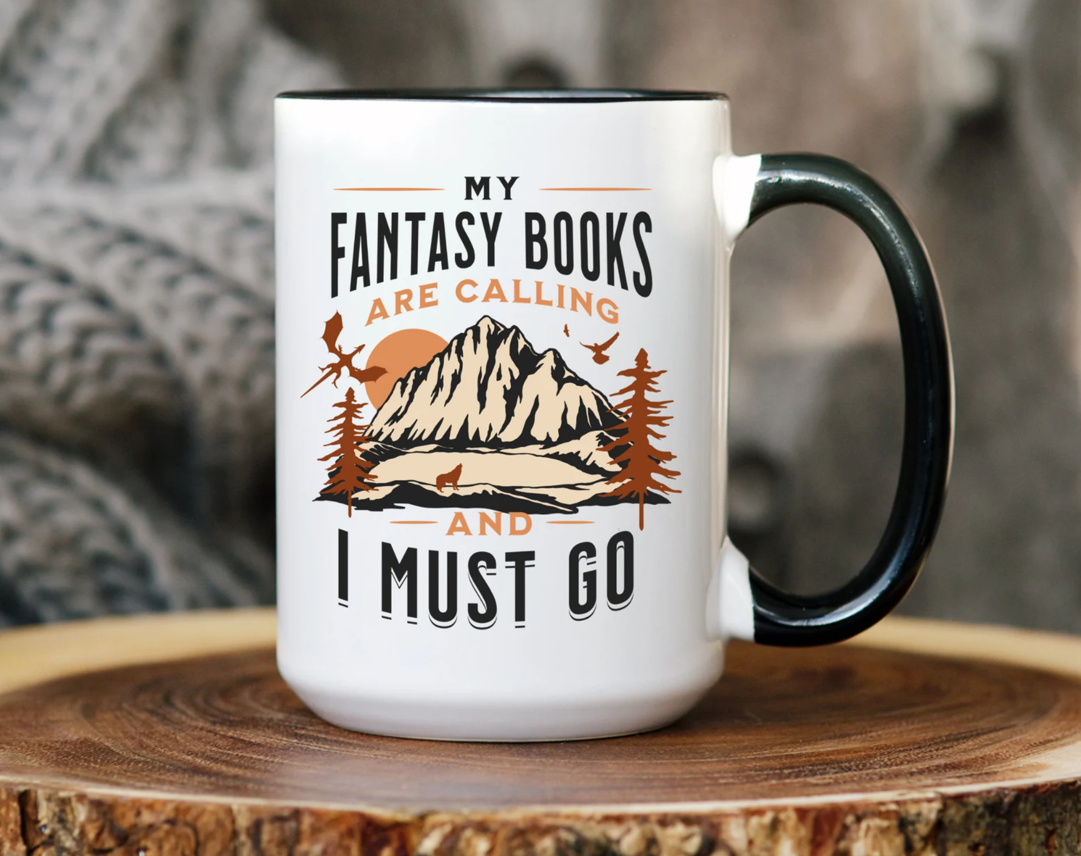 White mug with black handle and an illustration of mountains that says "My fantasy books are calling and I must go."