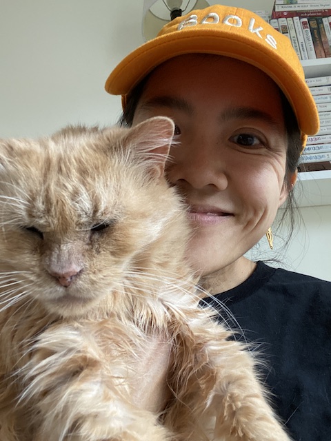 the author wearing a yellow hat that says "Books" and holding her tabby cat