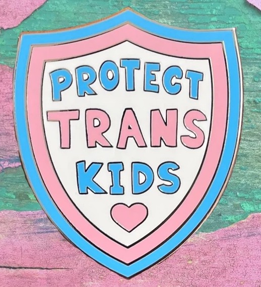 an enamel pin shaped like a badge in trans pride colors with the text Protect Trans Kids