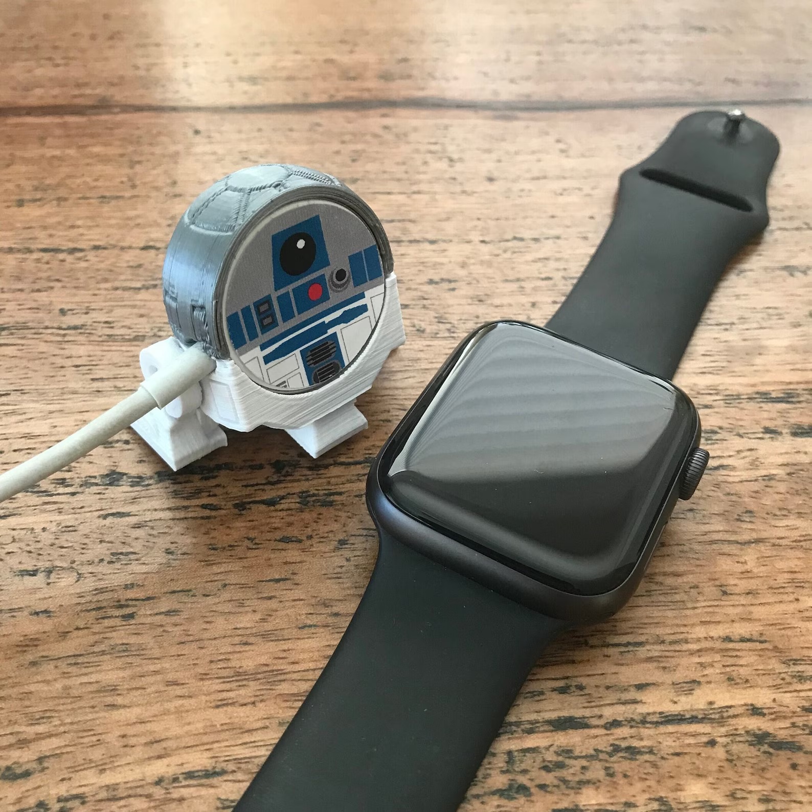 A R2D2-shaped Apple Watch charger cover, next to an Apple Watch for scale