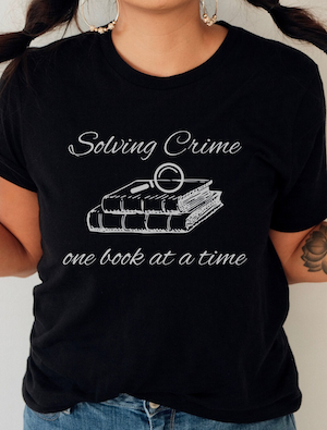 black tshirt with a graphic of books and a magnifying glass with text saying "solving crime one book at a time"