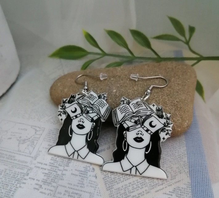 Image of a pair of black and white earrings. They feature a head covered in open books.