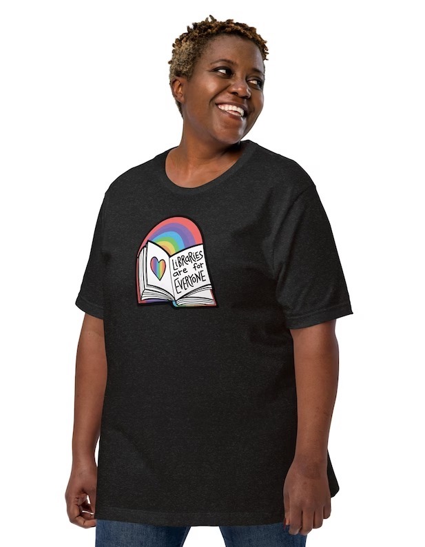 a photo of someone wearing a black shirt that says Libraries Are for Everyone with a book and a rainbow