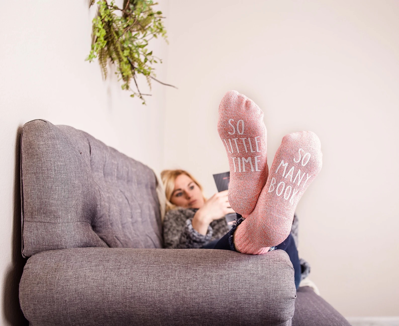 a photo of a white woan wearing a pair of pink socks. The socks say "so little time" and "so many books"