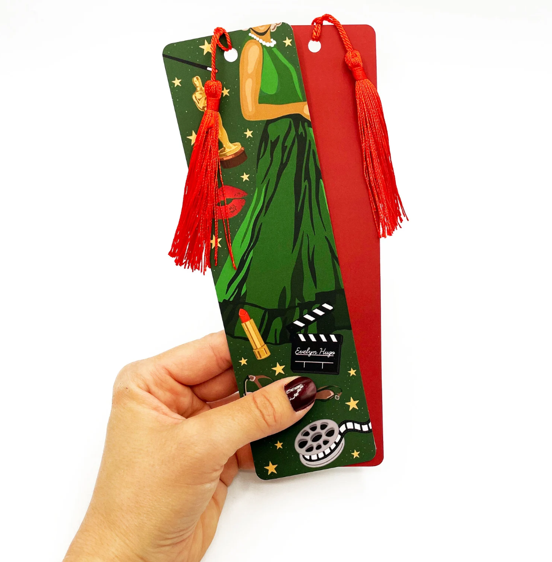 Green bookmark with red tassel and back featuring illustrations of a woman in a green dress, lipstick, an old film reel, and other images inspired by the novel The Seven Husbands of Evelyn Hugo