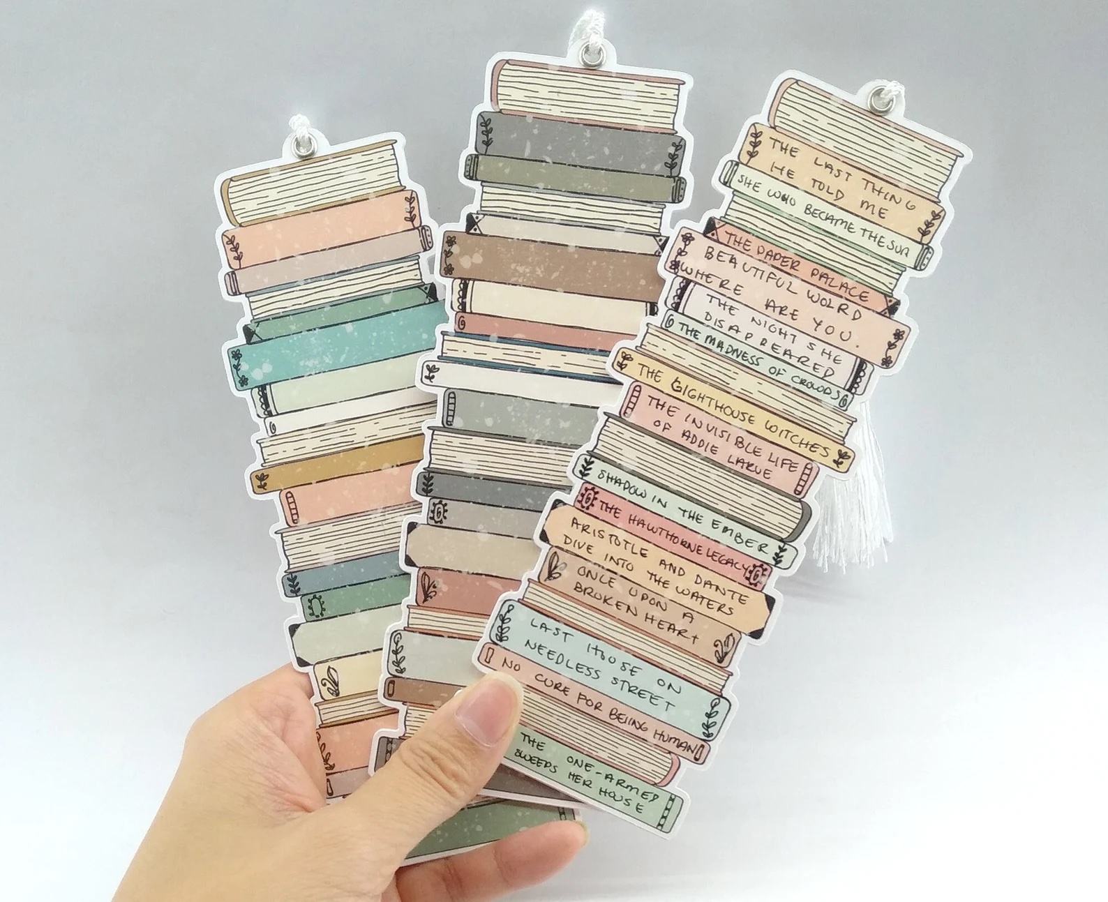 a photo of a white hand holding three bookmarks made up of stacked books