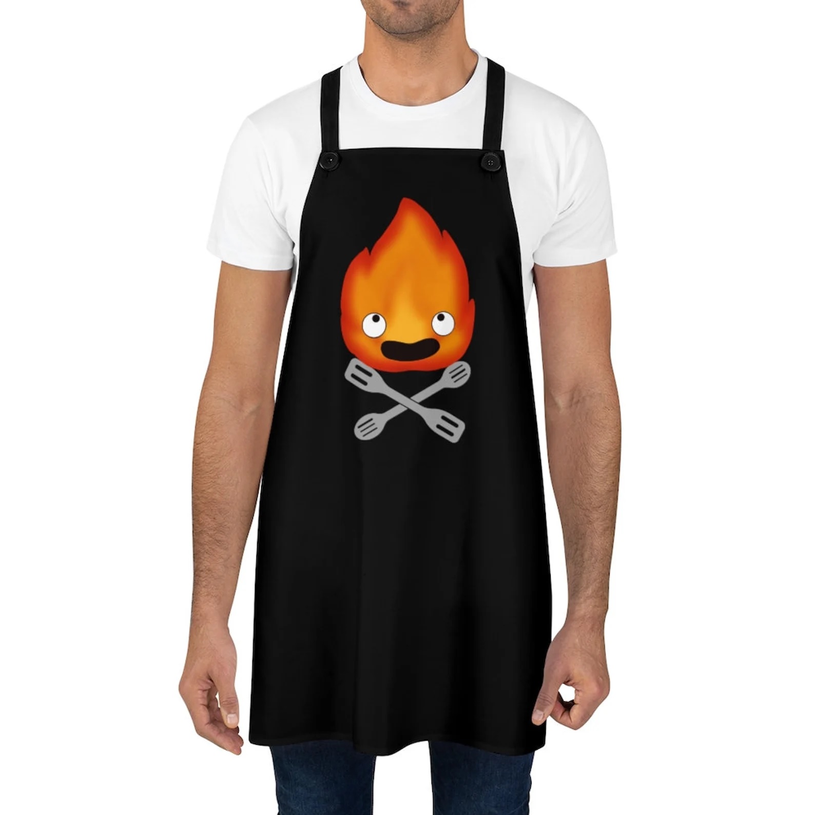 A black apron with an image of Calcifer above a pair of crossed spatulas