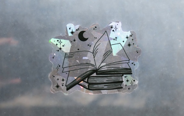 Image of a suncatcher sticker that is an open book on a stack of books.