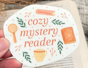 cover image for a sticker that says "cozy mystery reader" with illustrations of books, mug, magnifying glass