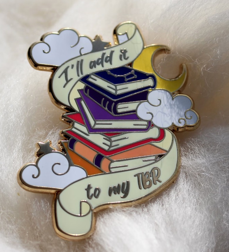 an enamel pin with a stack of rainbow colored books and the text "I'll aadd it to my TBR."