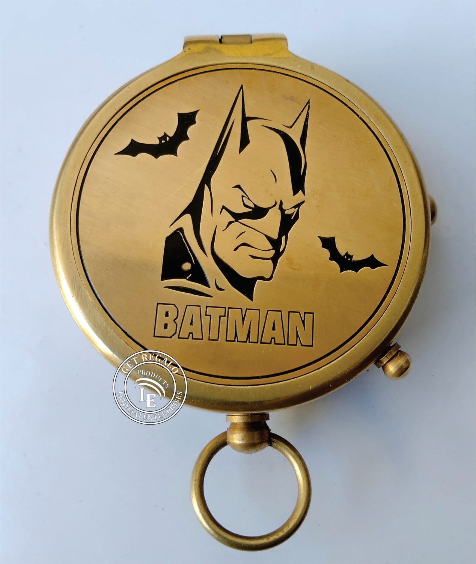 A closed brass compass with an engraved image of Batman's head and a couple of bats