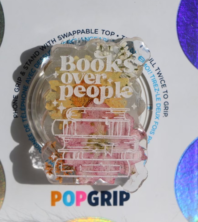 phone grip that says "books over people" with colorful flowers in the background. 