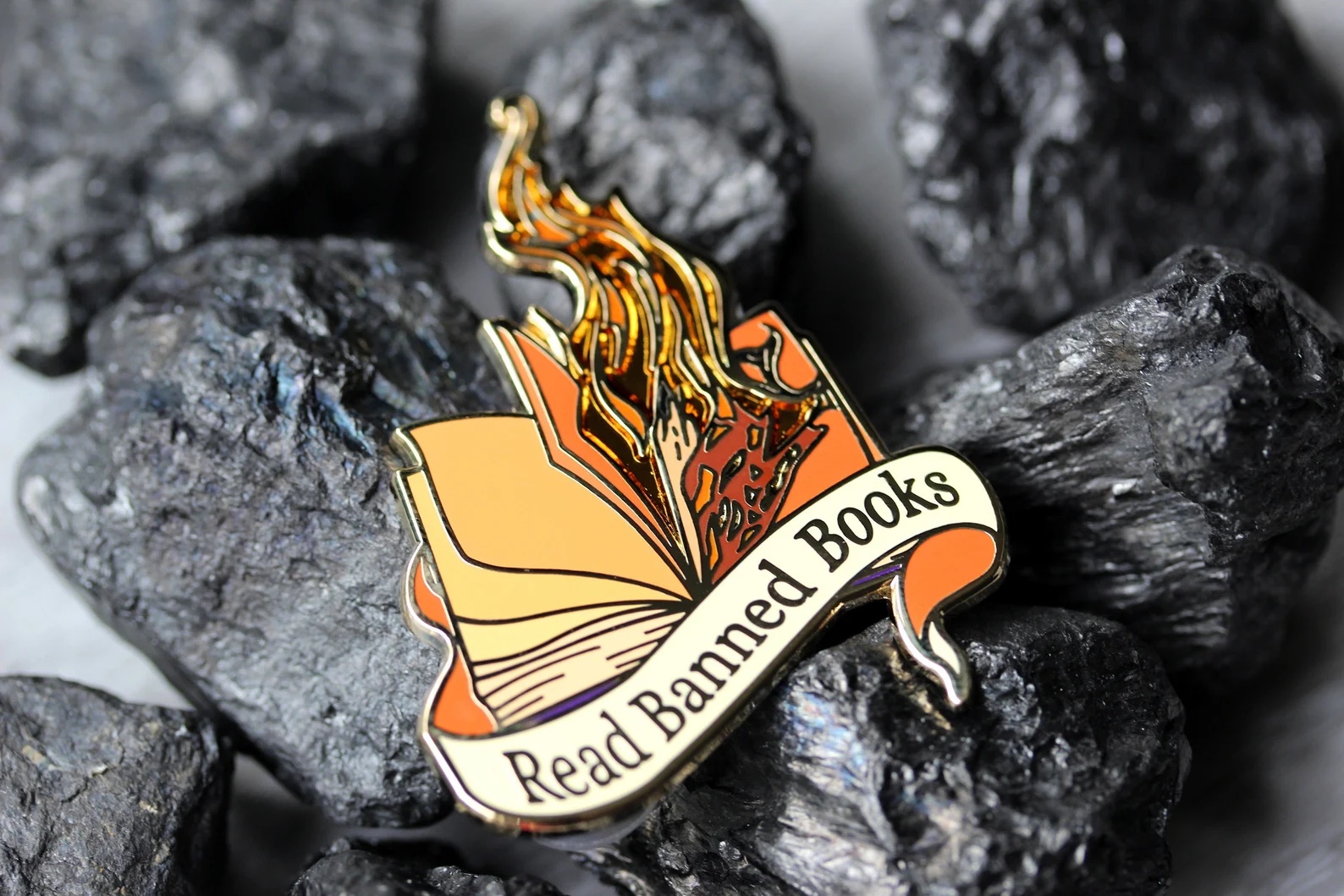 a photo of an enamel pin that features a book on fire and the phrase "Read Banned Books