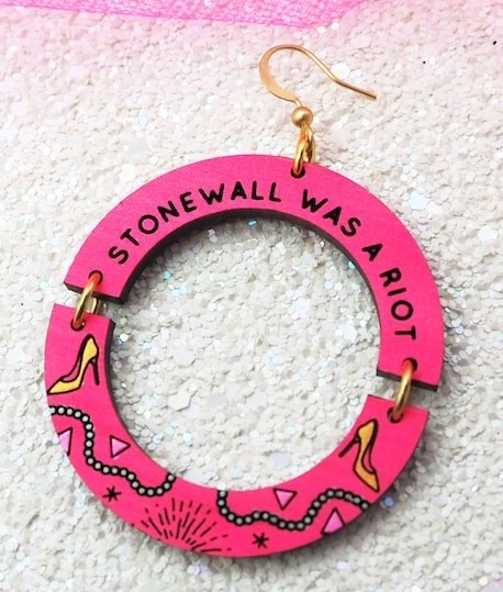 a round pink earring with the text Stonewall is a riot