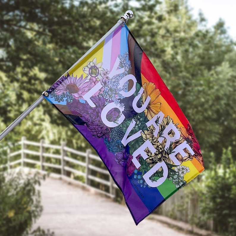 a photo of a progress Pride flag with flower illustrations and the text You Are Loved