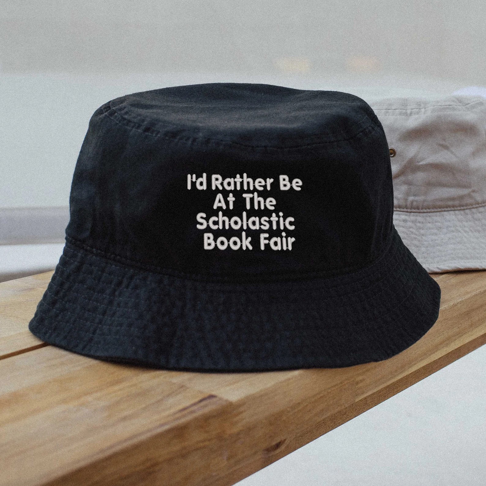 a photo of a black bucket hat that has white words that say, "I'd Rather Be At the Scholastic Book Fair"