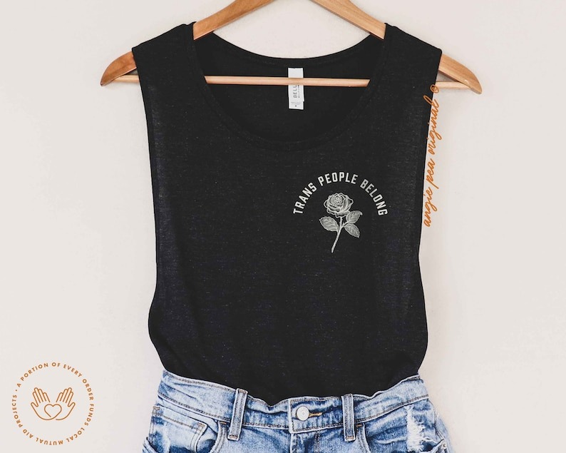 a black tank top with the text Trans People Belong above a rose illustration