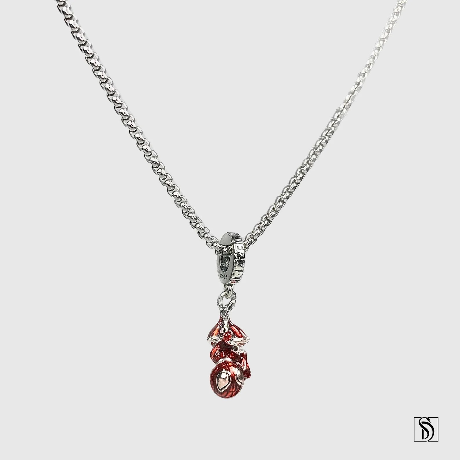 A silver chain necklace with a pendant of Spider-Man hanging upside-down